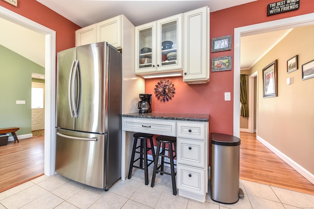 kitchen with baseboards, light tile patterned flooring, freestanding refrigerator, white cabinets, and glass insert cabinets