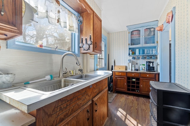 kitchen featuring brown cabinetry, wallpapered walls, a sink, light countertops, and dark wood-type flooring