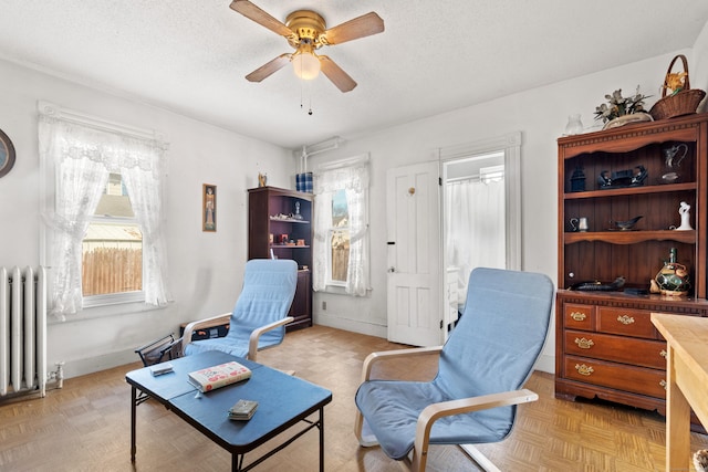 living area with ceiling fan, radiator, baseboards, and a textured ceiling