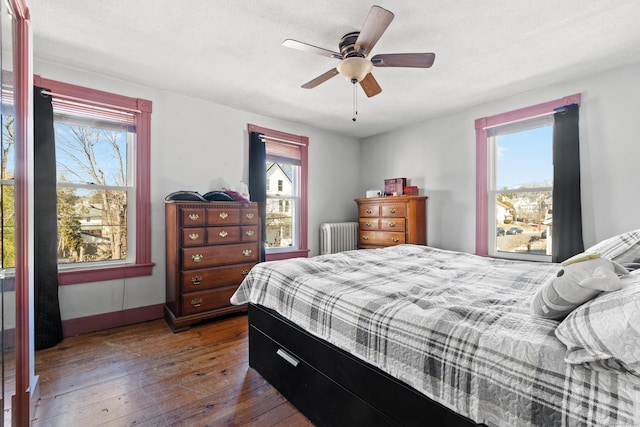 bedroom with baseboards, wood-type flooring, radiator, and ceiling fan