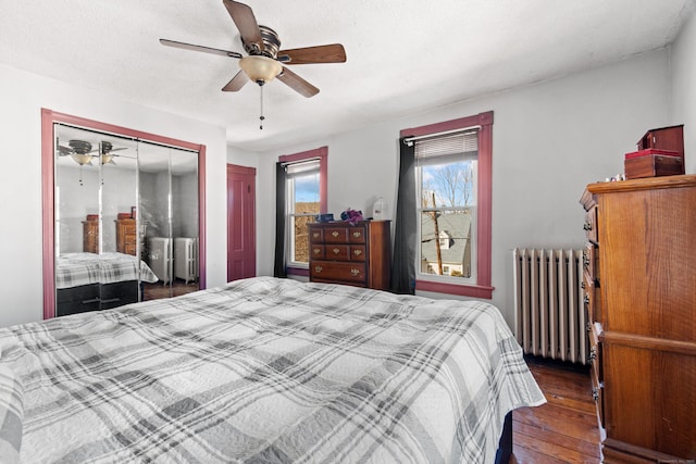 bedroom with a textured ceiling, dark wood-style floors, radiator heating unit, a closet, and ceiling fan