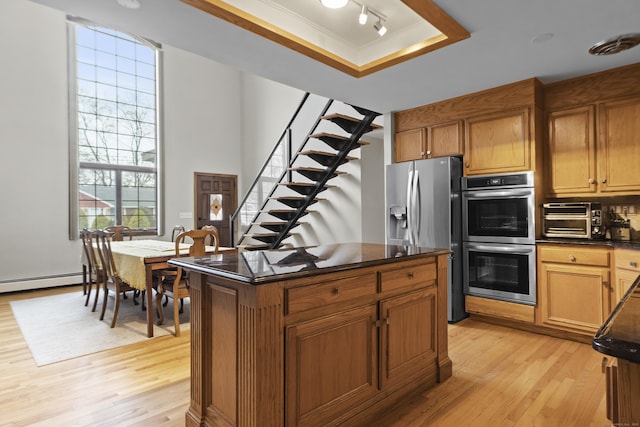 kitchen with a tray ceiling, light wood-style flooring, a toaster, stainless steel appliances, and dark countertops