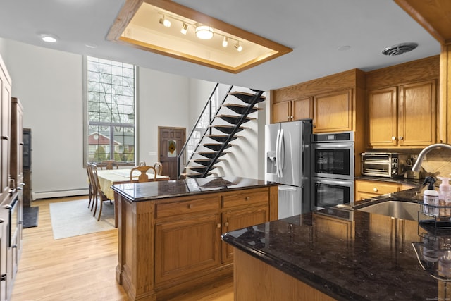 kitchen featuring a tray ceiling, a sink, appliances with stainless steel finishes, brown cabinets, and baseboard heating