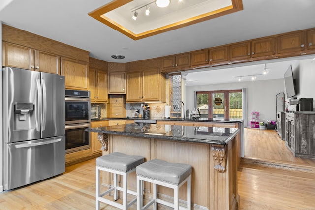 kitchen with a tray ceiling, a kitchen island, stainless steel appliances, light wood finished floors, and decorative backsplash