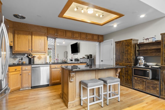 kitchen featuring a tray ceiling, a kitchen breakfast bar, light wood-style flooring, and stainless steel appliances