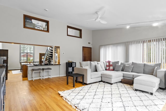 living room featuring light wood finished floors, stairway, high vaulted ceiling, a ceiling fan, and a baseboard radiator