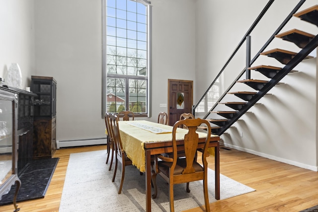 dining space featuring wood finished floors, baseboards, a high ceiling, stairs, and baseboard heating