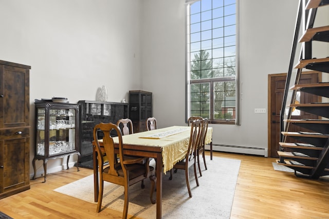 dining room with baseboard heating, stairs, light wood-style floors, and a towering ceiling