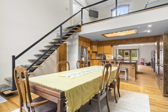 dining room with stairway, recessed lighting, light wood-style floors, and a towering ceiling