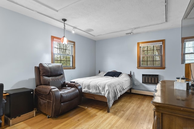 bedroom with multiple windows, a textured ceiling, a wall unit AC, and light wood finished floors