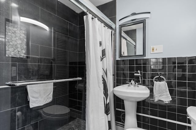 bathroom featuring tiled shower, toilet, and tile walls