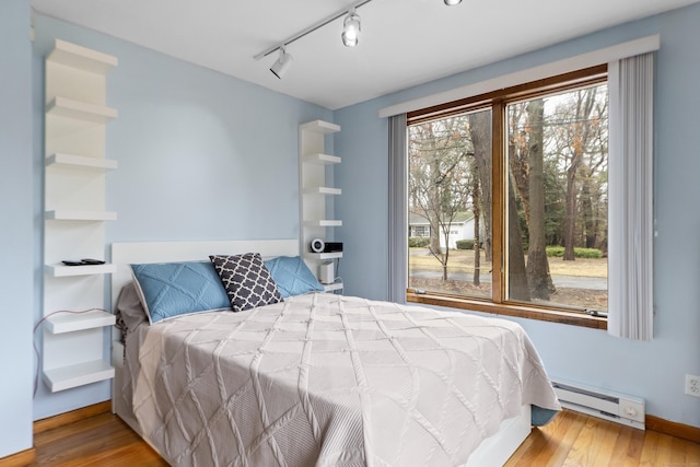 bedroom featuring a baseboard heating unit, wood finished floors, and baseboards