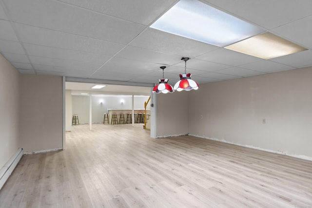 interior space with a drop ceiling, baseboard heating, and light wood-style flooring