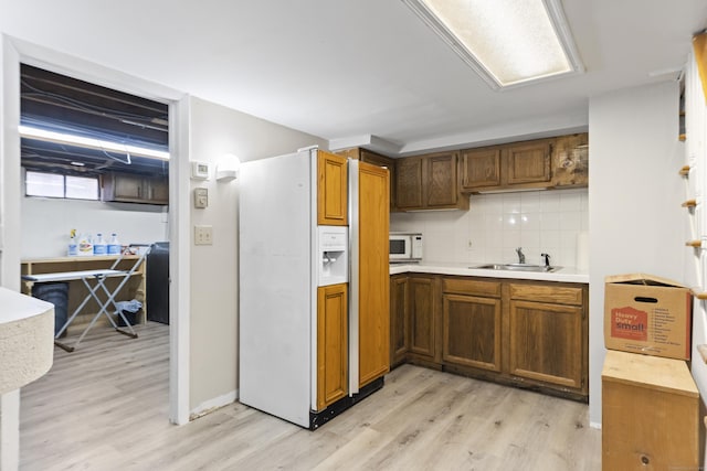 kitchen with tasteful backsplash, brown cabinets, light wood-style floors, white appliances, and a sink