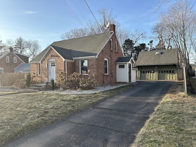 view of side of home with aphalt driveway, an outdoor structure, an attached garage, brick siding, and a chimney