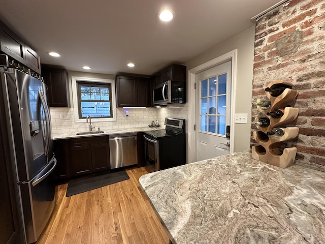 kitchen with a sink, light wood-style flooring, light stone counters, and stainless steel appliances