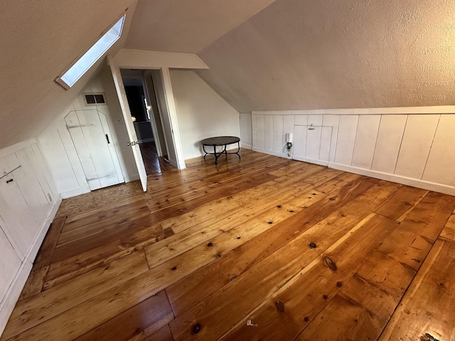 additional living space featuring visible vents, vaulted ceiling with skylight, and hardwood / wood-style floors