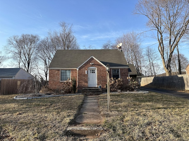 view of front facade with brick siding, a front lawn, and fence