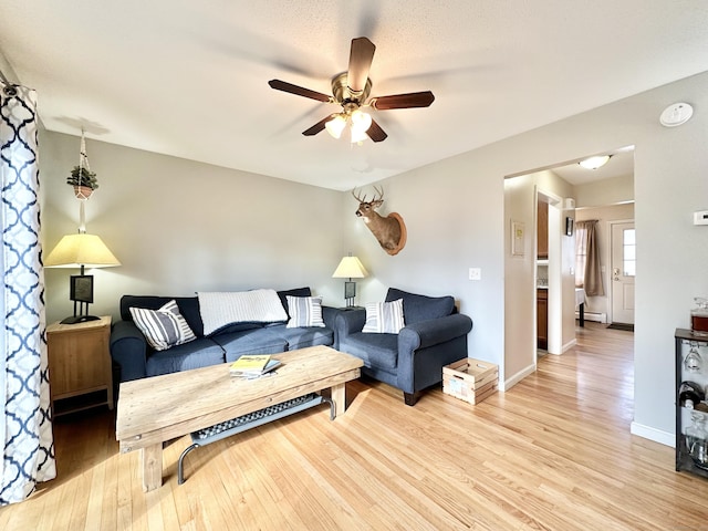 living room with a baseboard heating unit, baseboards, light wood-style floors, and ceiling fan