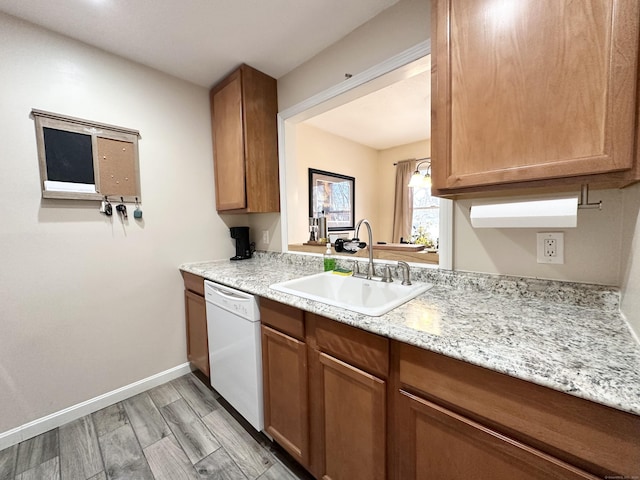 kitchen with light wood-style flooring, a sink, brown cabinetry, baseboards, and dishwasher