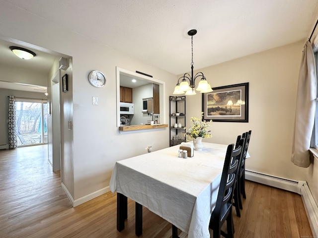 dining space featuring a notable chandelier, baseboard heating, a baseboard heating unit, and wood finished floors