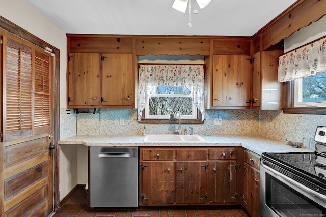 kitchen with a sink, tasteful backsplash, appliances with stainless steel finishes, light countertops, and brick floor