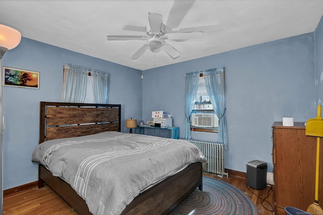 bedroom featuring radiator, ceiling fan, baseboards, cooling unit, and wood finished floors