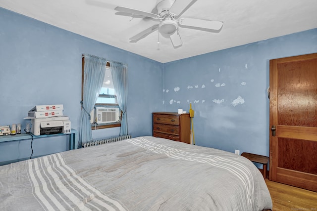 bedroom with a ceiling fan, radiator, wood finished floors, and cooling unit