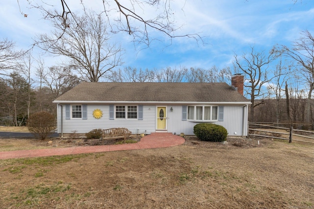 ranch-style home with a front yard, a shingled roof, a chimney, and fence