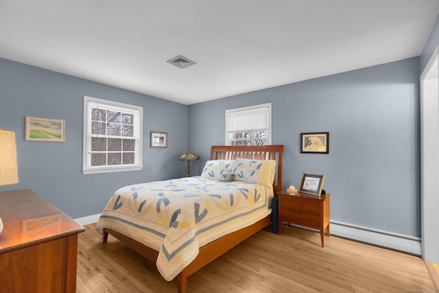 bedroom with a baseboard heating unit, light wood-style flooring, baseboards, and visible vents