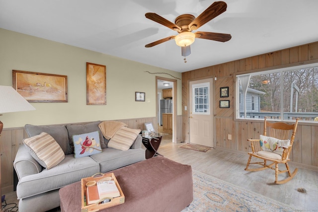 living area with wainscoting, wood finished floors, a ceiling fan, and wood walls