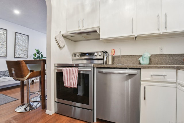 kitchen featuring under cabinet range hood, appliances with stainless steel finishes, white cabinetry, and wood finished floors