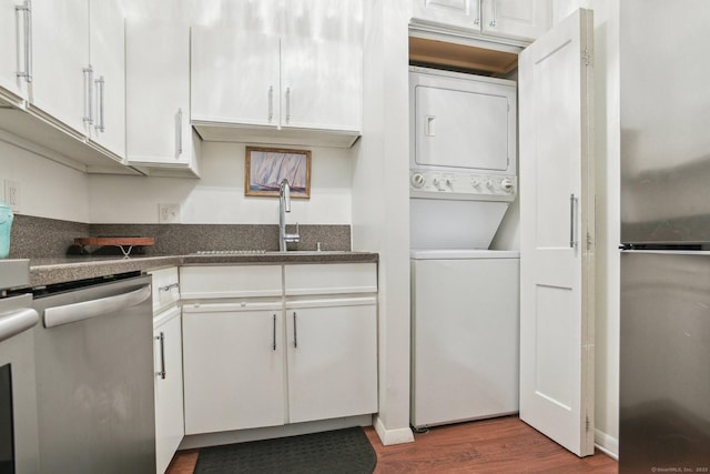 kitchen with stainless steel dishwasher, stacked washer and dryer, white cabinetry, and a sink