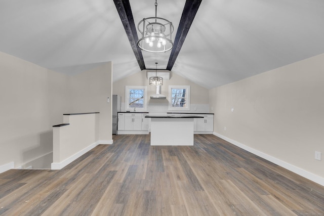 kitchen with a notable chandelier, dark countertops, dark wood finished floors, white cabinets, and wall chimney range hood