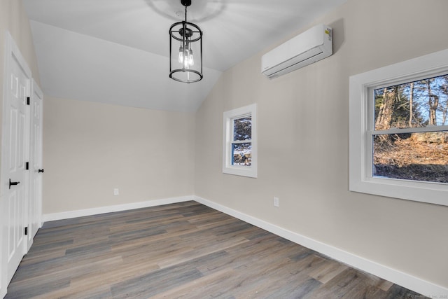 spare room featuring an AC wall unit, wood finished floors, baseboards, and vaulted ceiling