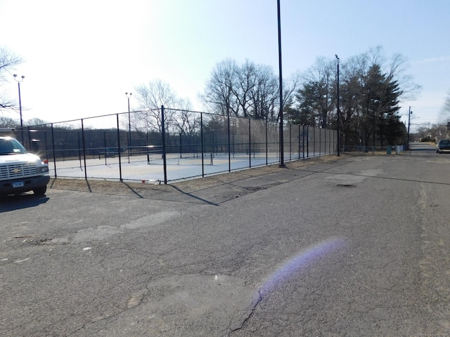 view of parking featuring a tennis court and fence