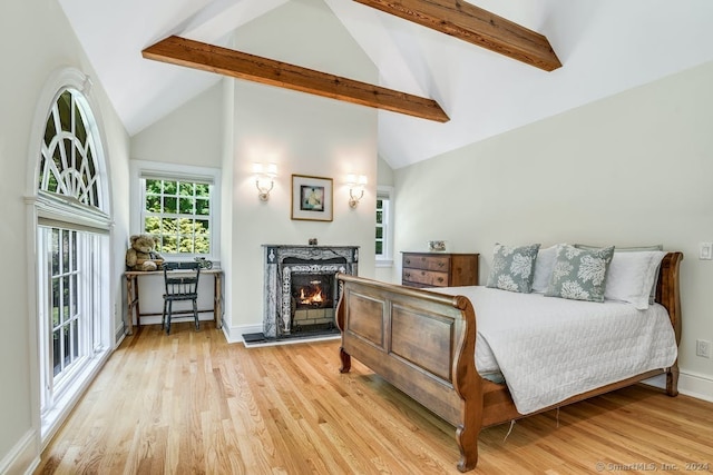 bedroom featuring a premium fireplace, beam ceiling, baseboards, and wood finished floors