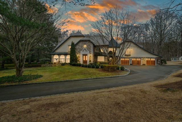 view of front of property featuring a garage, a lawn, stone siding, and driveway