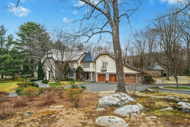 view of front of home with a standing seam roof, aphalt driveway, stone siding, an attached garage, and metal roof