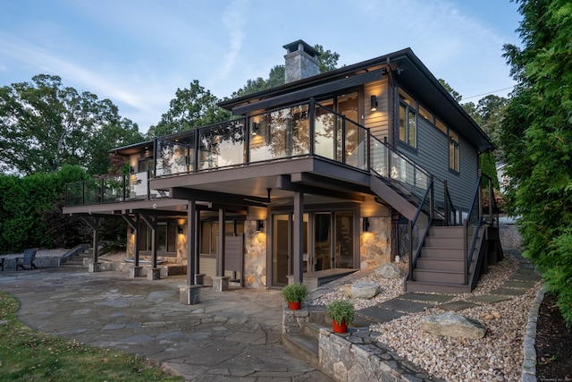 rear view of house with stairs, a patio area, stone siding, and a chimney