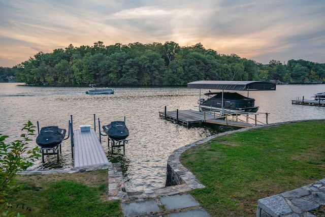 dock area with a yard, a water view, boat lift, and a view of trees