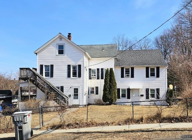 view of front of house featuring a fenced front yard, roof with shingles, a chimney, and stairway