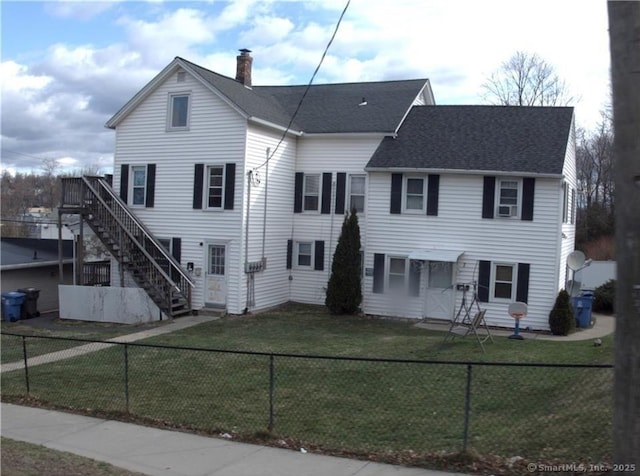 view of front of home with a fenced front yard, stairway, a front yard, roof with shingles, and a chimney