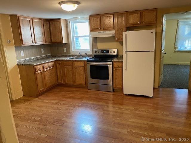 kitchen featuring dark countertops, under cabinet range hood, stainless steel range with electric stovetop, freestanding refrigerator, and a sink