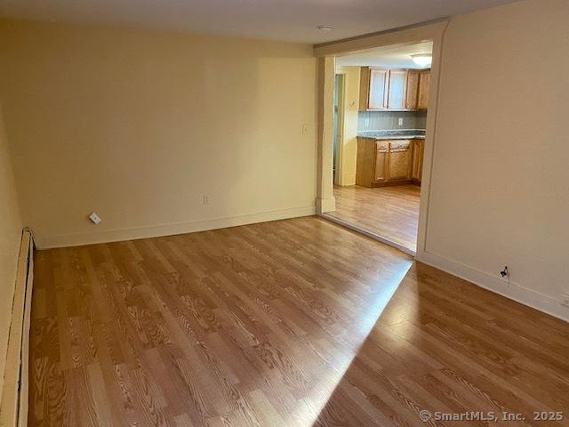 spare room with a baseboard heating unit, wood finished floors, and baseboards