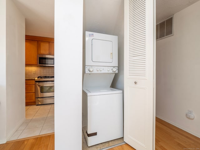 clothes washing area featuring visible vents, baseboards, stacked washer and dryer, laundry area, and light wood-style flooring