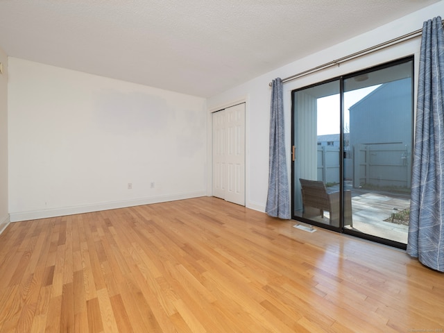 empty room with baseboards, light wood finished floors, and a textured ceiling