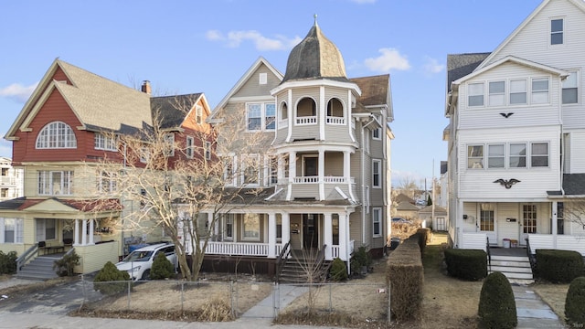 view of front of house with a porch, a balcony, a fenced front yard, and a chimney