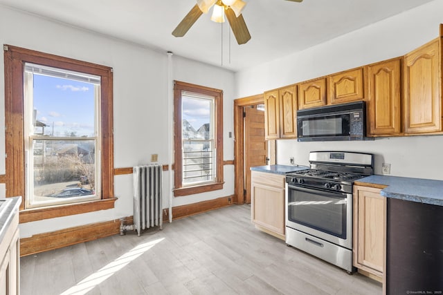 kitchen featuring radiator heating unit, a healthy amount of sunlight, black microwave, and stainless steel gas range oven