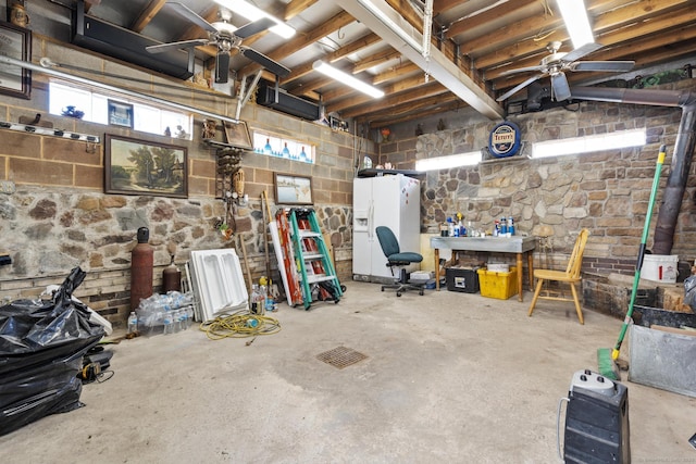 below grade area with a ceiling fan and white fridge with ice dispenser